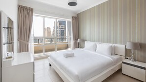 Habitación de hotel moderna con una cama grande, una mesita de noche con lámpara, una ventana con cortinas y vistas a la ciudad.