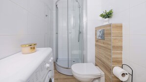 Une salle de bain moderne dotée d’une douche à parois de verre, de toilettes et d’un lave-linge.