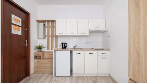 Une cuisine compacte avec des meubles blancs, un petit réfrigérateur, un évier et une machine à café.