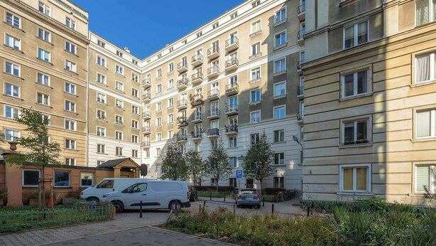 Ein mehrgeschossiges Wohngebäude mit Balkonen, einem Parkplatz und einem kleinen Garten.