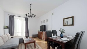 Ein modernes Wohnzimmer mit einer Couch, einem Esstisch für vier Personen, einem Fernseher und einer Deckenleuchte.