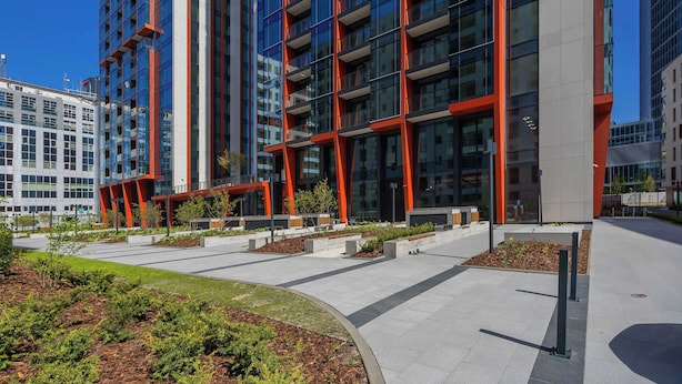 Un bâtiment moderne doté d’une façade en verre et de touches de couleur rouge, entouré d’espaces paysagers et d’un chemin piétonnier.