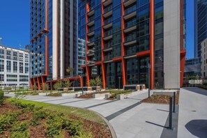 Un bâtiment moderne doté d’une façade en verre et de touches de couleur rouge, entouré d’espaces paysagers et d’un chemin piétonnier.