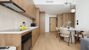 Une cuisine moderne avec des meubles en bois, un four encastré et un coin repas comprenant une table ronde et des chaises.