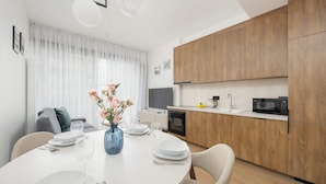 Une cuisine moderne avec des meubles en bois, un four à micro-ondes et un coin repas doté d’une table blanche, mise pour quatre personnes.