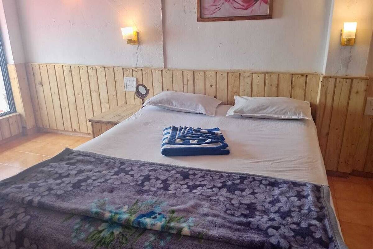 Een hotelkamer met een bed, kussens, een dekbed en een wandlamp.