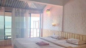 Ein Schlafzimmer mit einem großen Bett, einem Deckenventilator, einem Fenster mit Vorhängen und Meerblick.