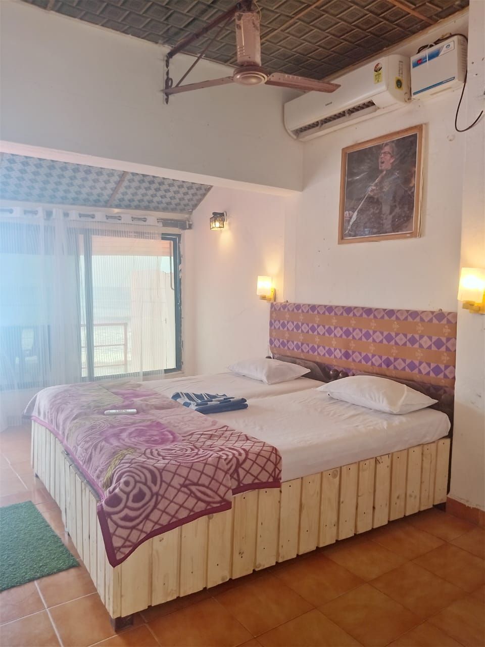 Un dormitorio con cama, ventilador de techo, aire acondicionado y ventana con cortinas.