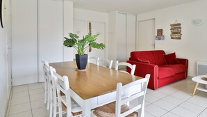 A modern living room with a wooden dining table, white chairs, a red sofa, and a potted plant. - Stylish Villa in Parentis-en-born (Parentis-en-Born)