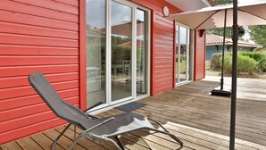 A red building with a sliding glass door, a wooden deck, and a single lounge chair. - Stylish Villa in Parentis-en-born (Parentis-en-Born)