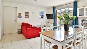 A living room with a red sofa, a dining table with white chairs, a TV, and a large window with curtains. - Stylish Villa in Parentis-en-born (Parentis-en-Born)