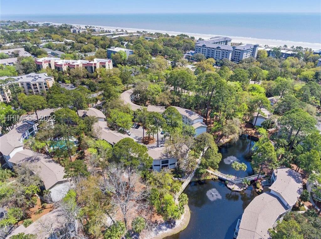 An aerial view of a resort area with multiple buildings, a body of water, and a beach in the background.