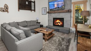 Un salon moderne avec un canapé gris, une table basse en bois, une cheminée et un téléviseur fixé au mur.