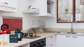 A modern kitchen with white cabinets, a red kettle, a gas stove, and a window with a view of a brick wall.