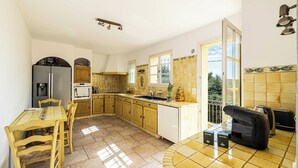 A kitchen with a dining table, chairs, a refrigerator, a sink, and a coffee machine. - A/C House 4br/10p With Pool - 40 min From Cannes (Le Tignet)