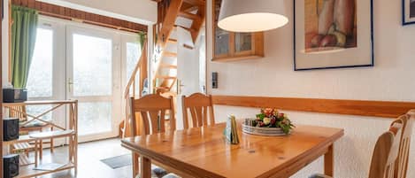 A dining area with a wooden table and chairs, a staircase, and a painting on the wall.
