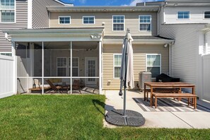 Une terrasse couverte avec une table et des chaises, un barbecue et une pelouse.
