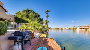 Un molo in legno che si protende sull'acqua calma, con un barbecue e una bombola di gas a sinistra e una tavola da paddleboard a destra.