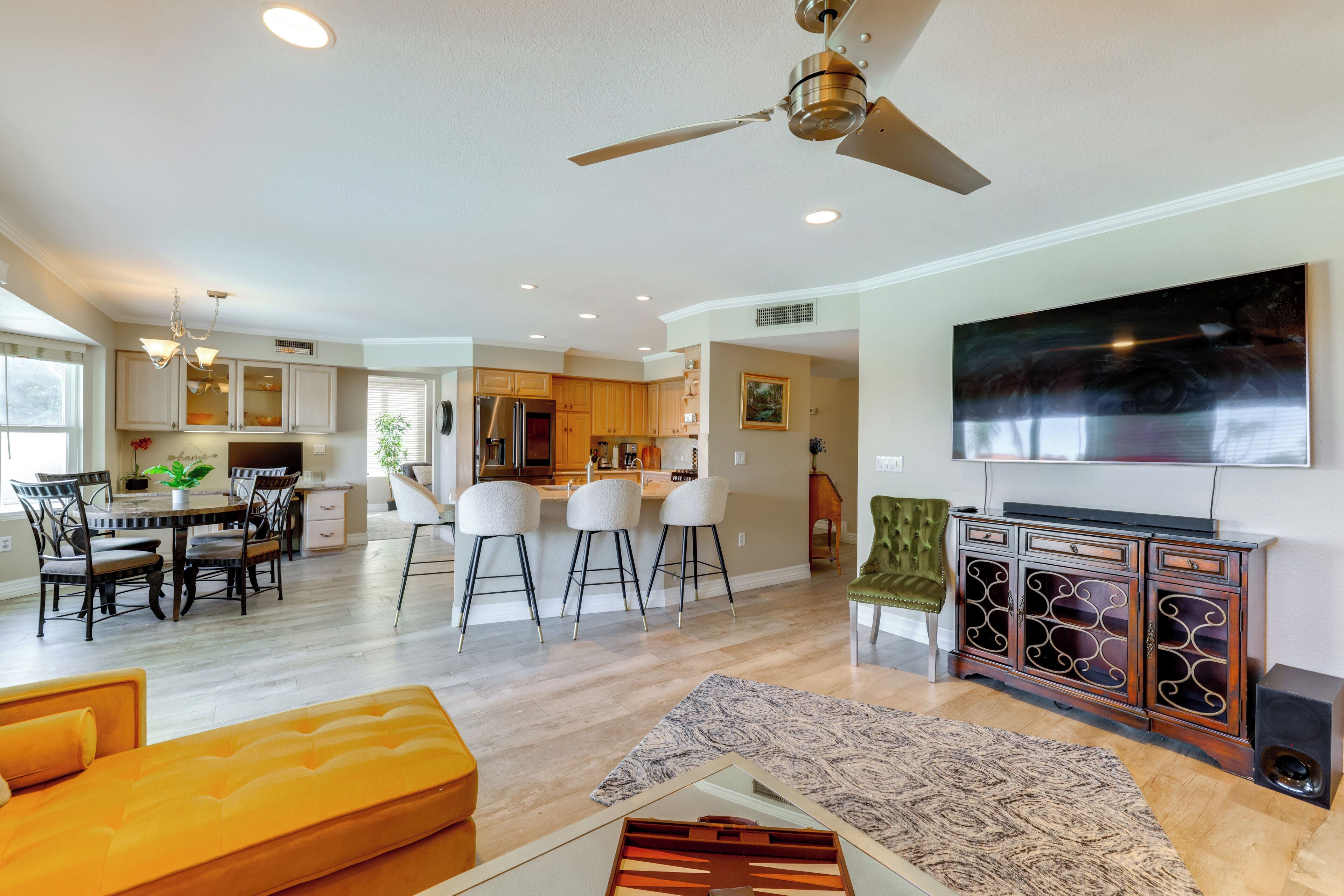 A modern living room with a sofa, a dining area with chairs, a kitchen with cabinets, and a ceiling fan.