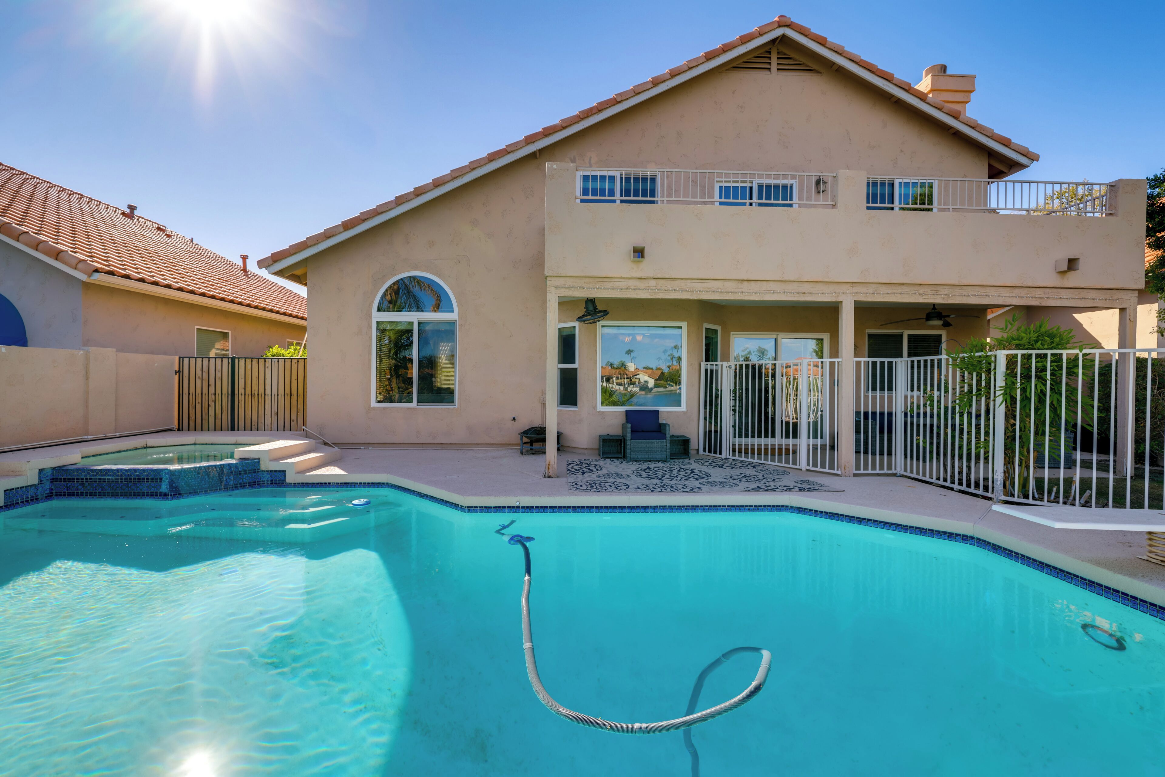 A two-story house with a swimming pool, a covered patio, and a fenced backyard.