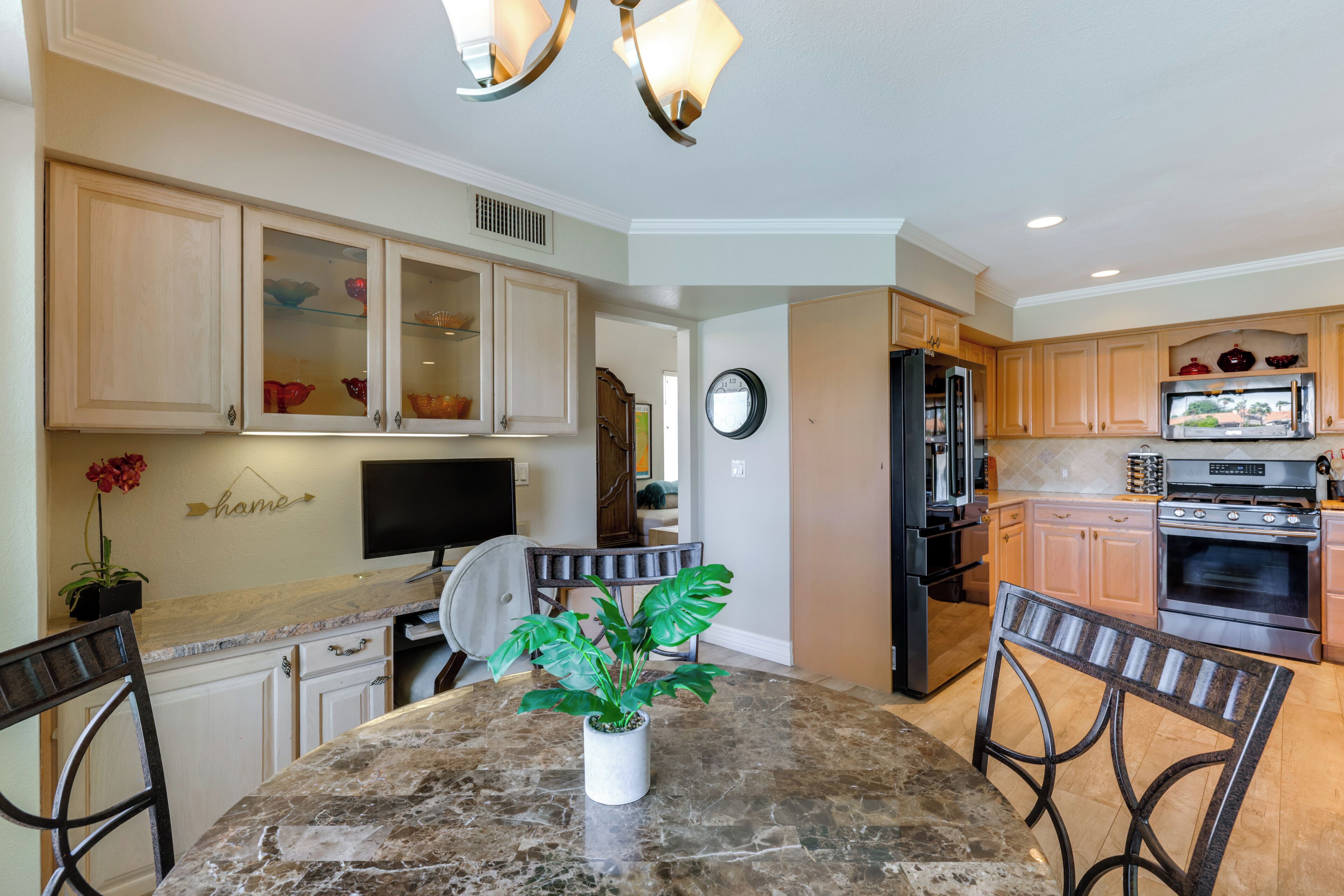 A kitchen with wooden cabinets, a marble countertop, a potted plant, and a dining area with chairs.