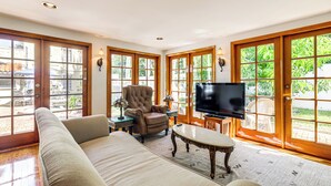 A living room with a sofa, armchair, television, and a view through large glass doors.