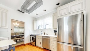 A modern kitchen with stainless steel appliances, white cabinetry, and a wooden floor.