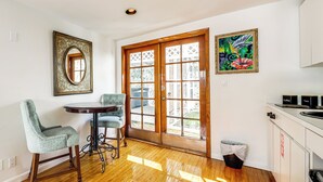 A dining area with a round table and two chairs, a wooden door with glass panels, and a painting on the wall.