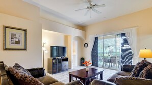 A living room with leather sofas, a coffee table, a TV, and a balcony with a view.