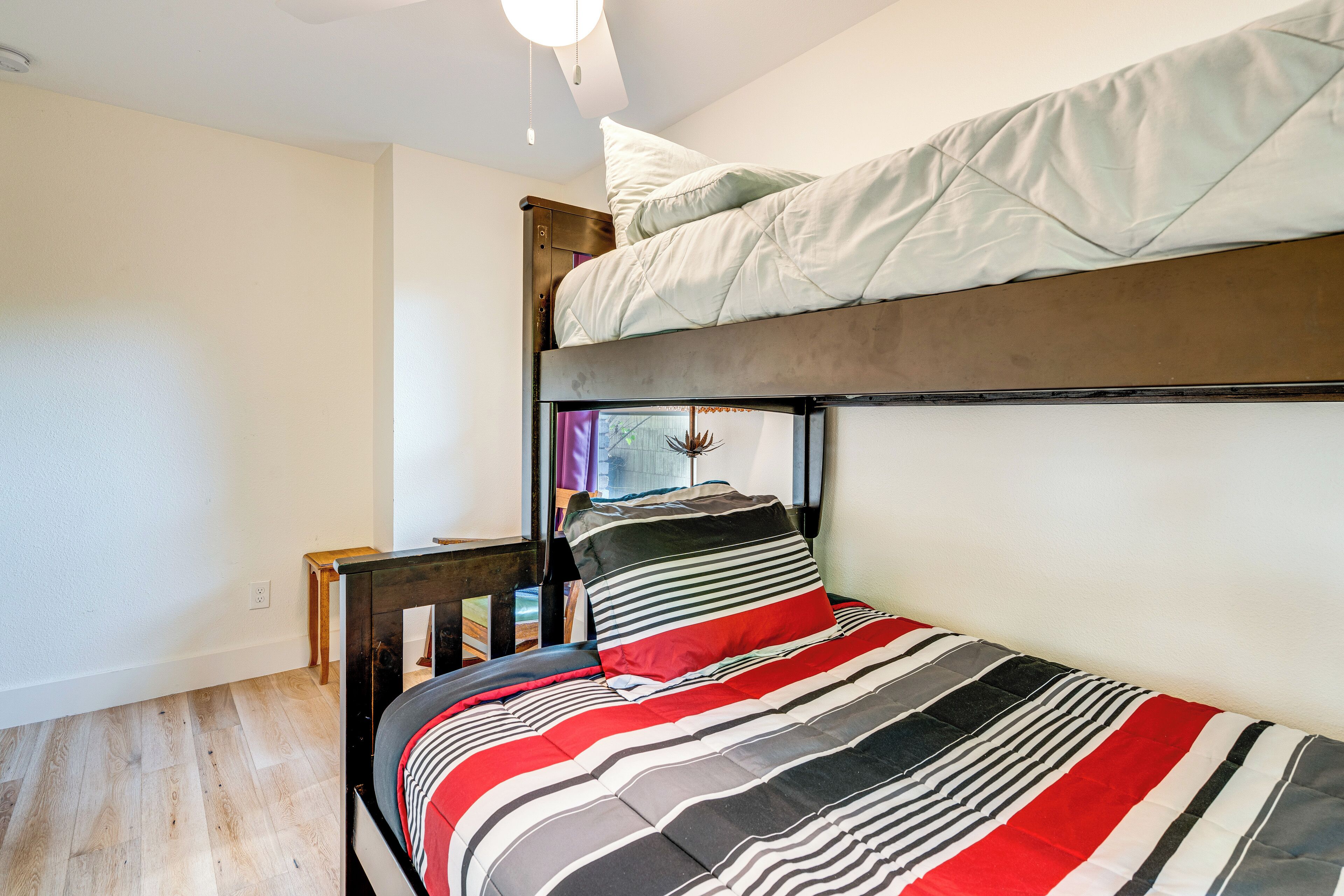 A bunk bed with a striped bedspread, a small wooden nightstand, and a window with curtains.
