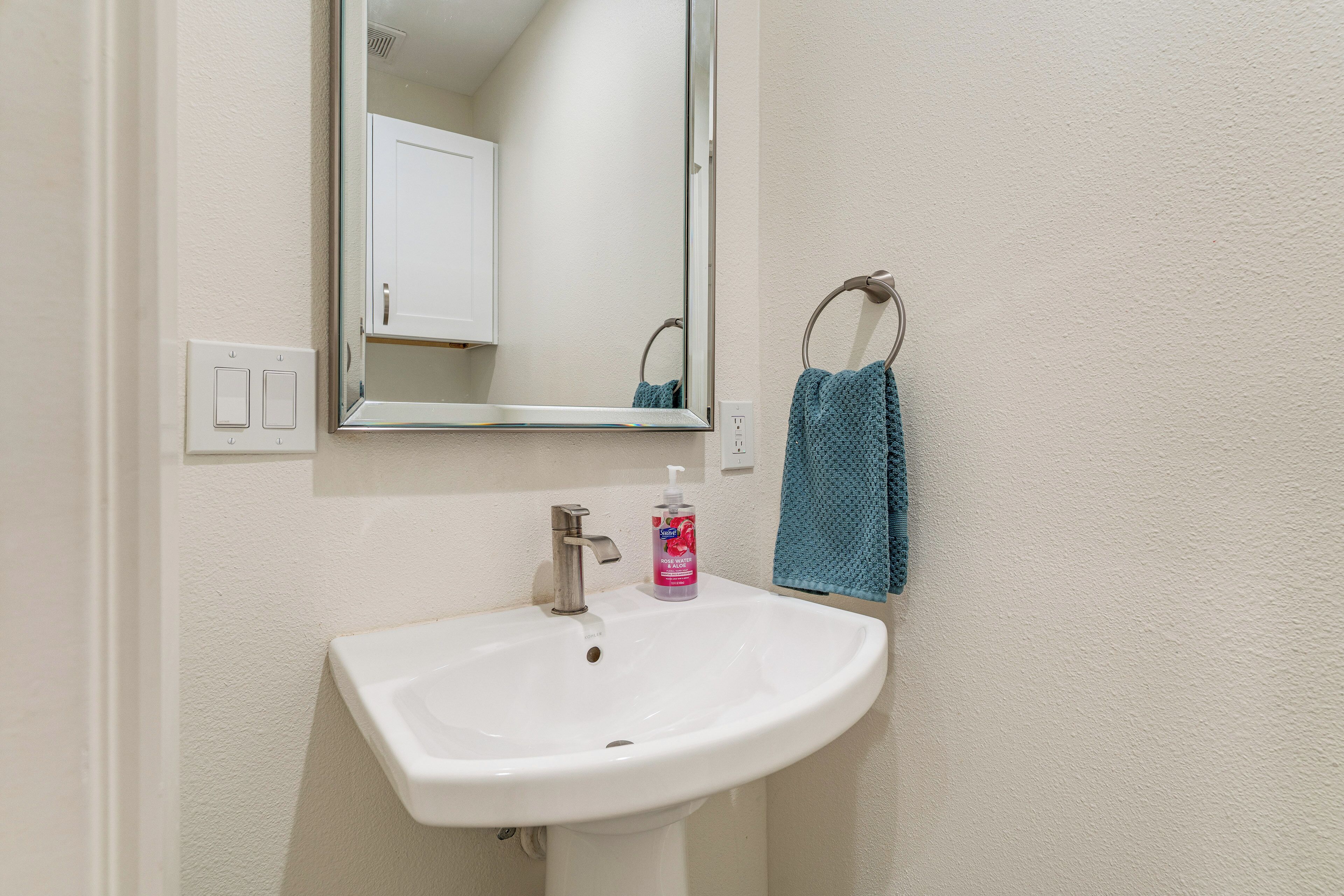 A bathroom with a white sink, a mirror, a towel ring, and a soap dispenser.