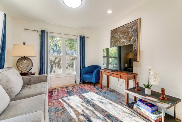 A living room with a sofa, a blue armchair, a TV, a desk, and a bookshelf. - 4 Mi to UT Austin: Bright & Modern Family Home (Austin)