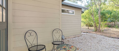 A patio with two metal chairs and a round table with a mosaic top, set against a beige wall with a small window.