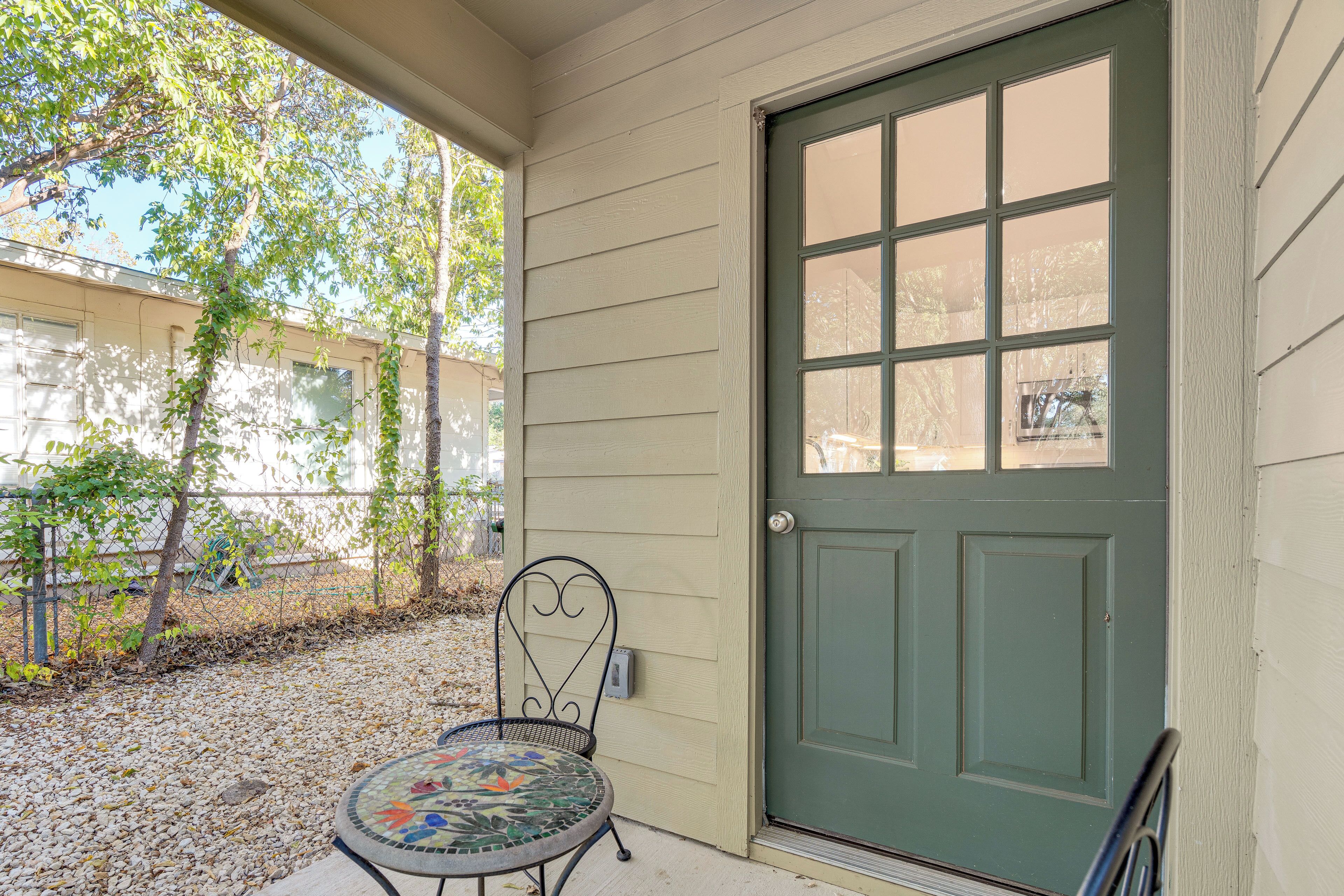 A green door with a window, a metal chair, and a mosaic table on a porch with gravel.