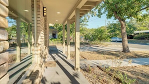 Un espace extérieur abrité, doté de murs en pierre, d’un chemin en béton et d’un arbre.