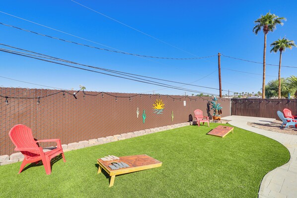 A backyard with artificial grass, a wooden table, and red chairs. - Pool, Games & Views! Lake Havasu City Family Home (Lake Havasu City)