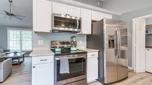 A modern kitchen with white cabinets, stainless steel appliances, and a dining area with a glass table and chairs. - Home w/ Pet-friendly Yard, 1 Mi to Dtwn Raleigh! (Raleigh)