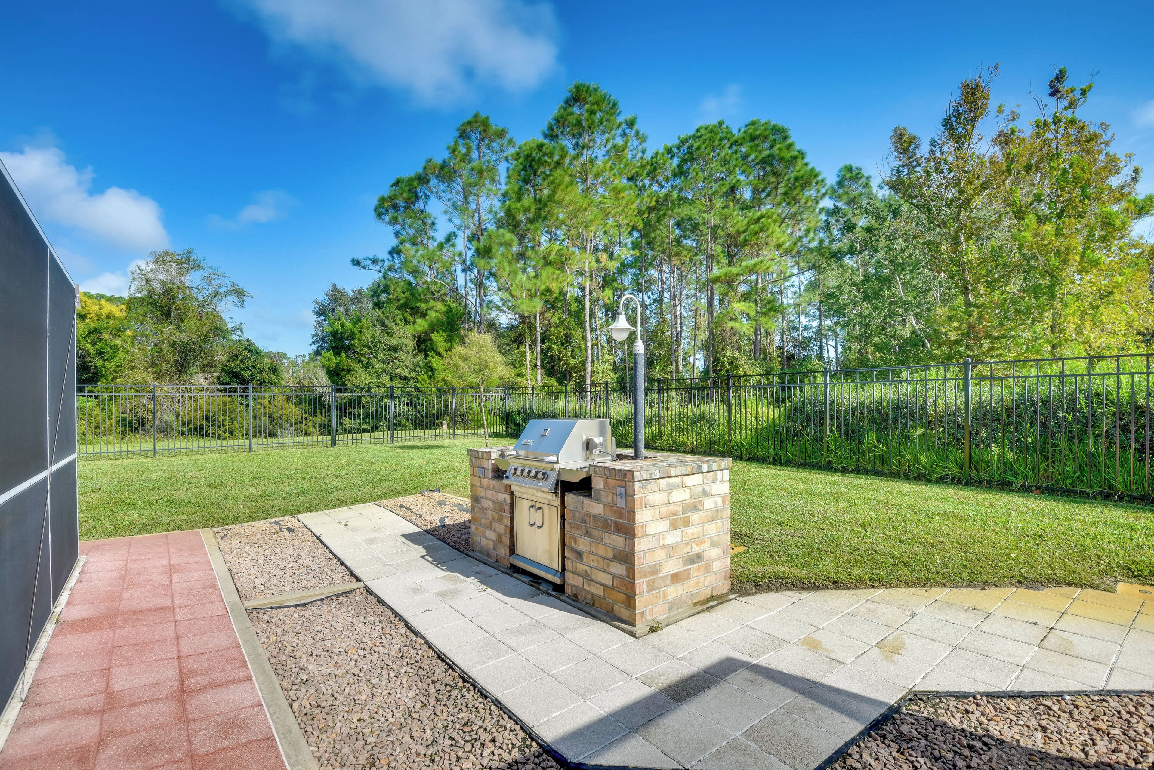 An outdoor barbecue area with a grill and seating, surrounded by a fenced yard and trees.