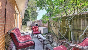 A patio with wicker furniture, a glass table, and a brick wall.