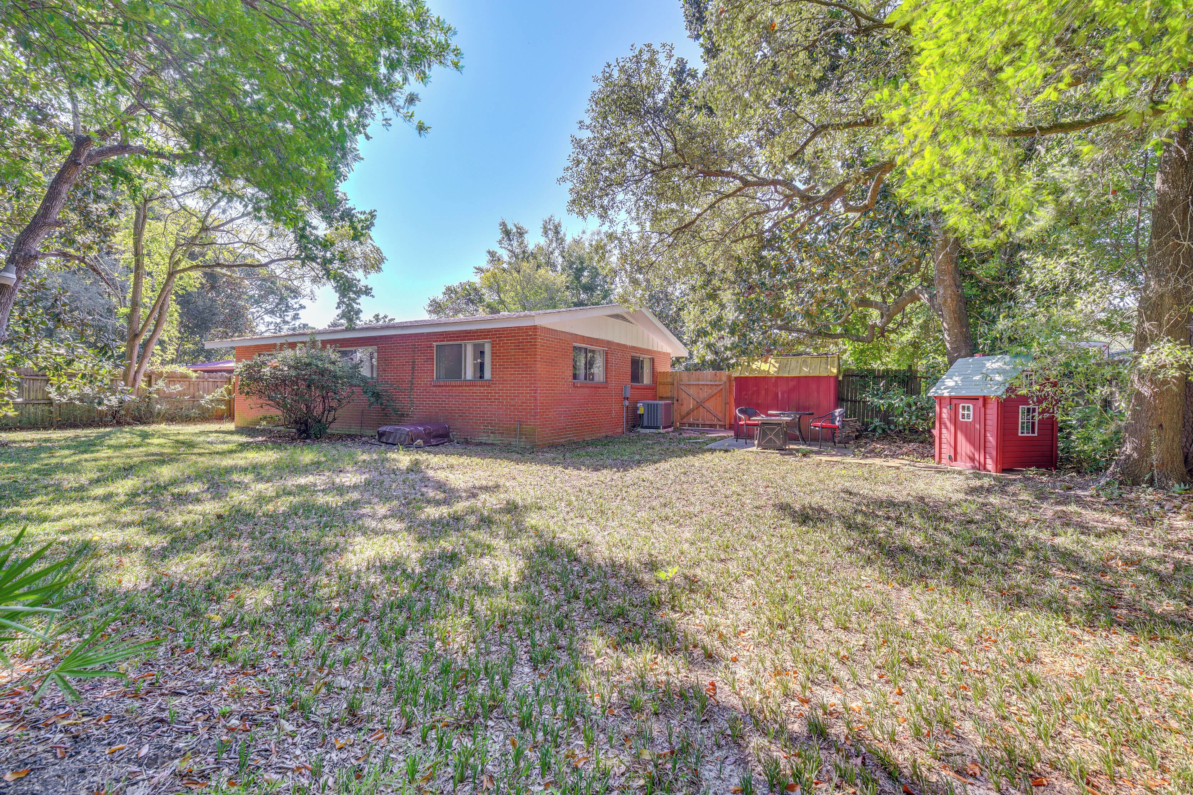 A single-story brick house with a small attached garage, surrounded by a grassy yard and trees.
