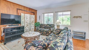 A living room with a sofa set, a television, a cabinet, and a window with a view of greenery.