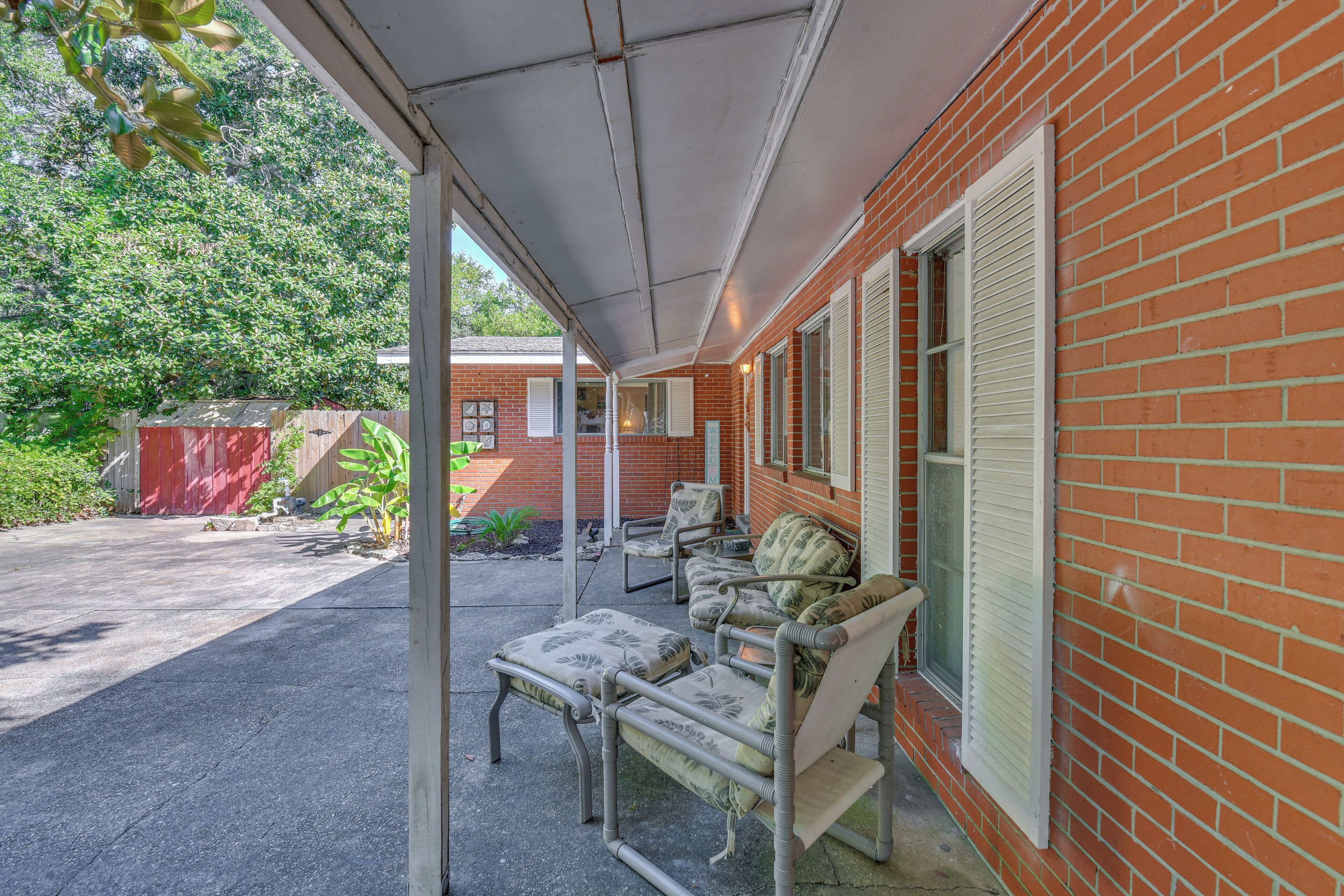 Ein überdachter Patio-Bereich mit Gartenmöbeln, ein Gebäude aus rotem Backstein und ein roter Schuppen im Hintergrund.