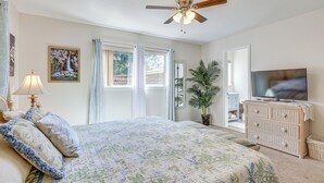 A bedroom with a bed, a ceiling fan, a television, a dresser, and a window with curtains.