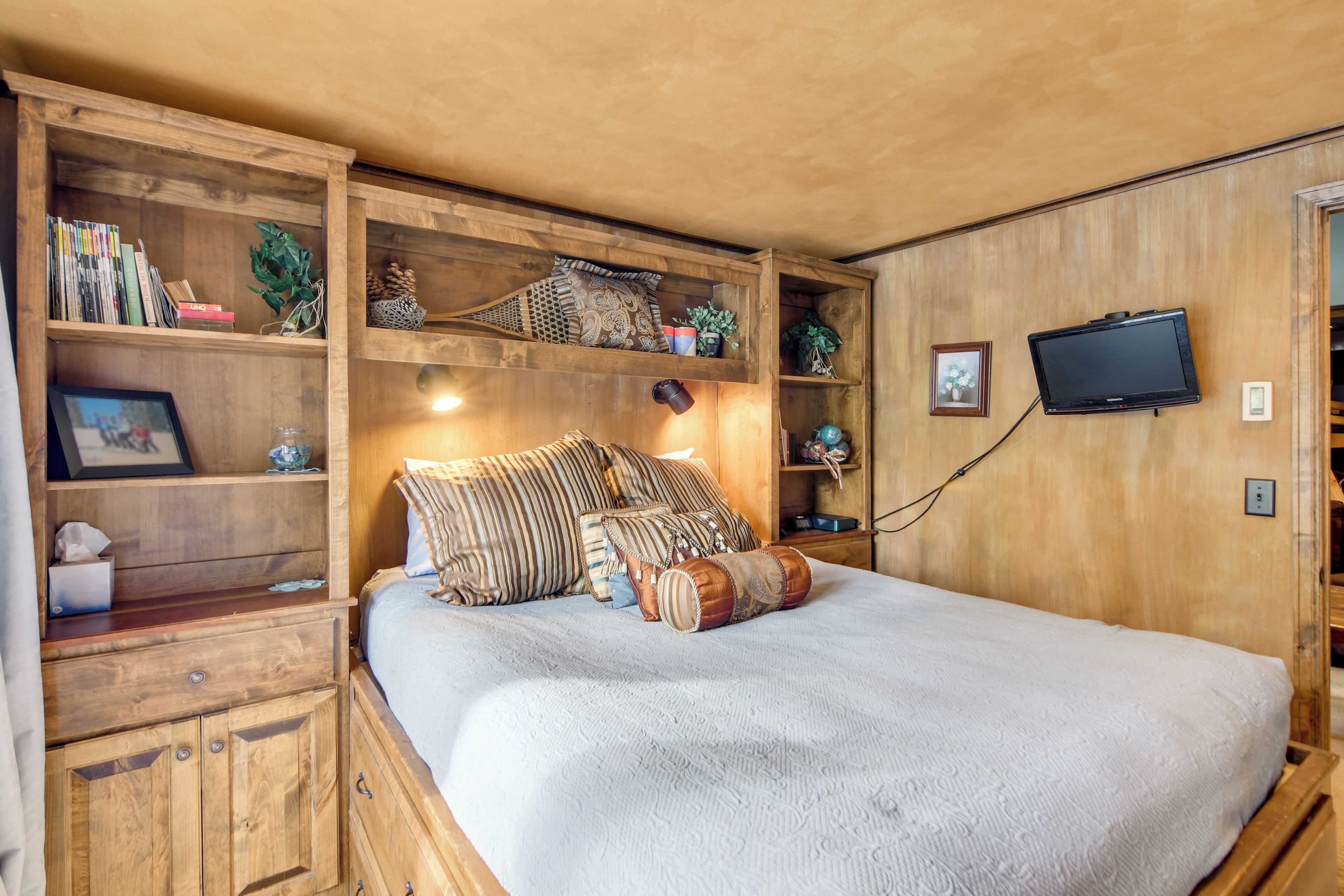 A bedroom with a large bed, wooden shelves, a television, and various decorative items.