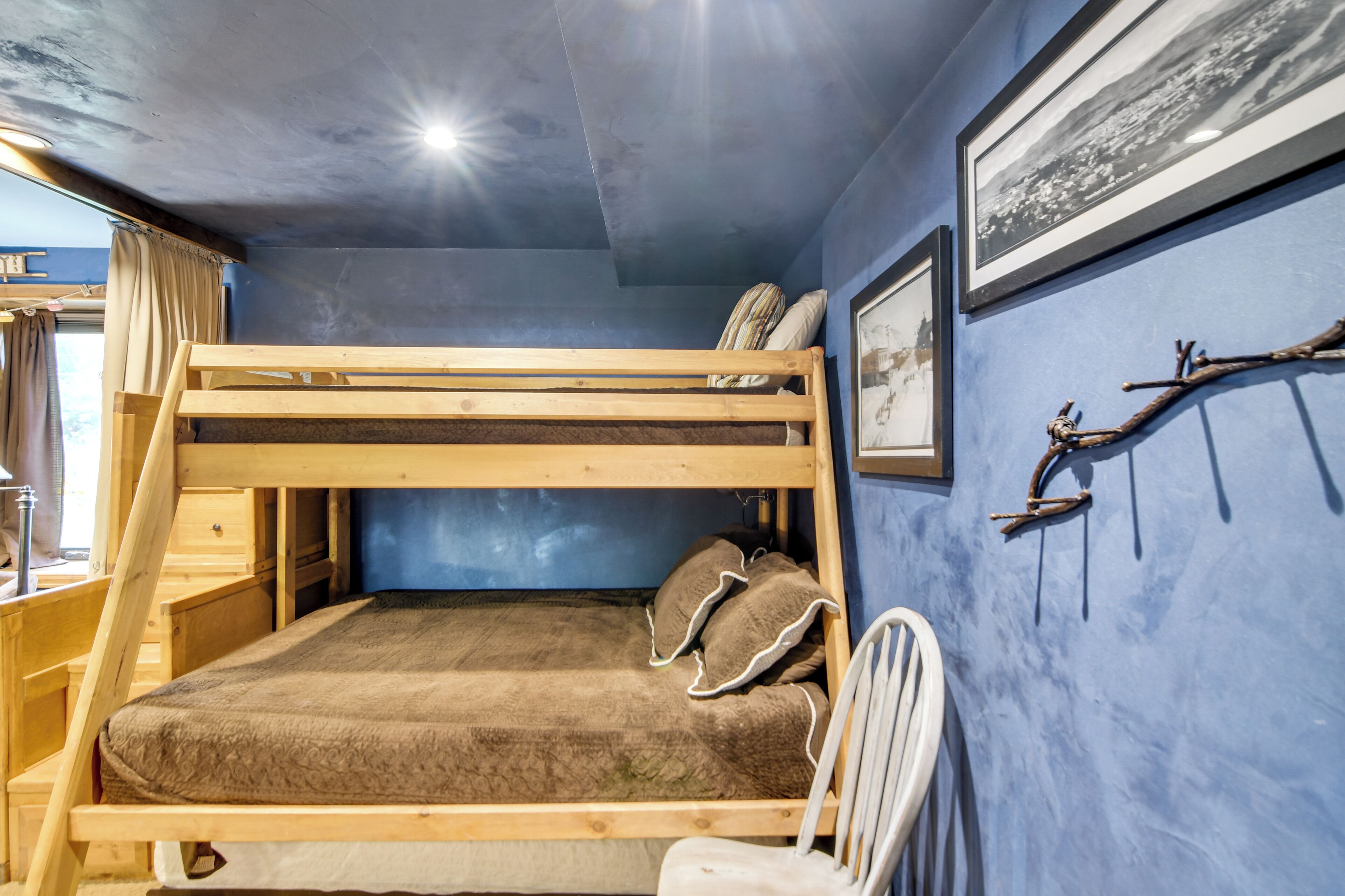 A bunk bed with a wooden frame and a mattress, a white chair, and a wall-mounted branch decoration.