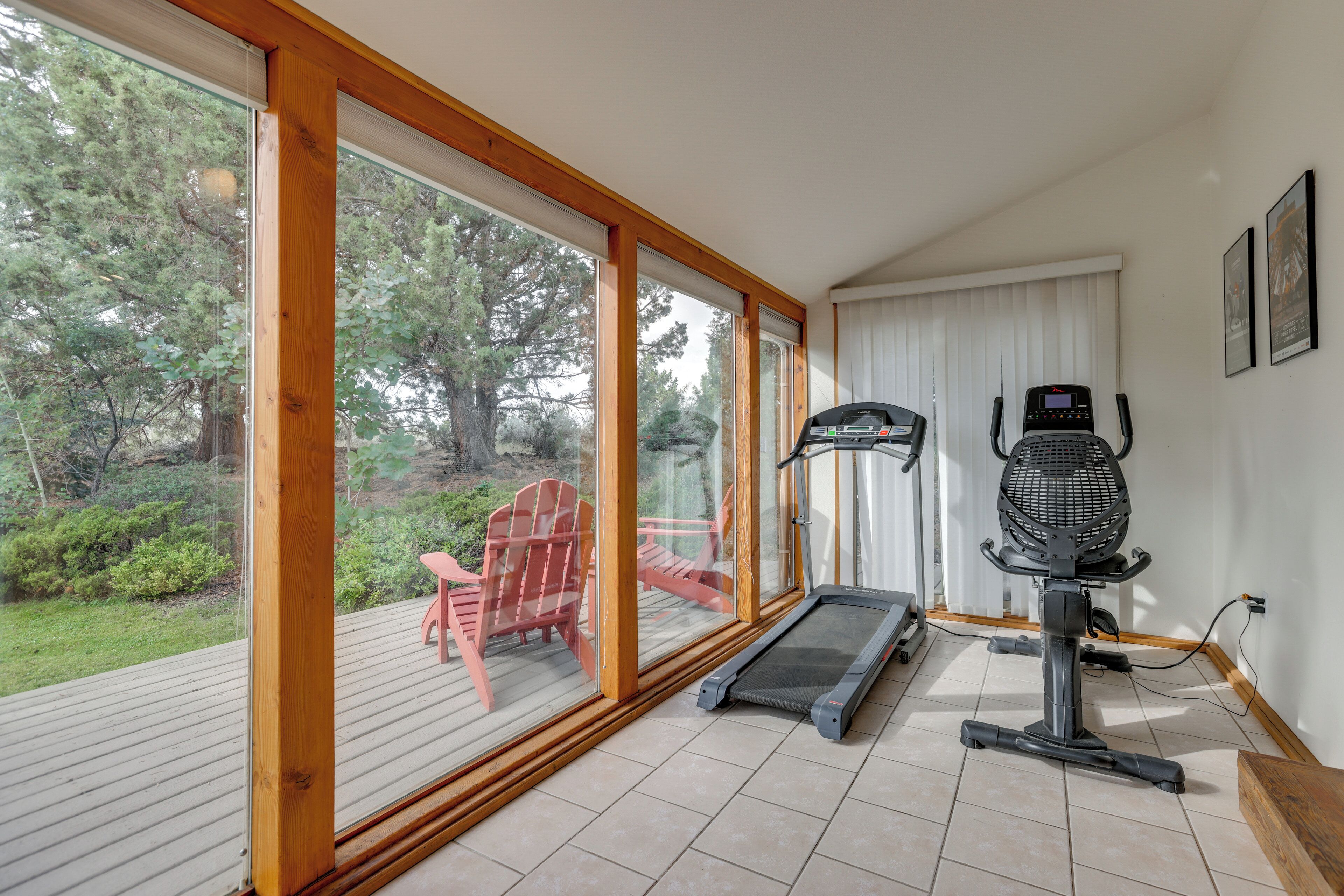 A gym with a treadmill, a stationary bike, and a red chair by a large window overlooking a deck.