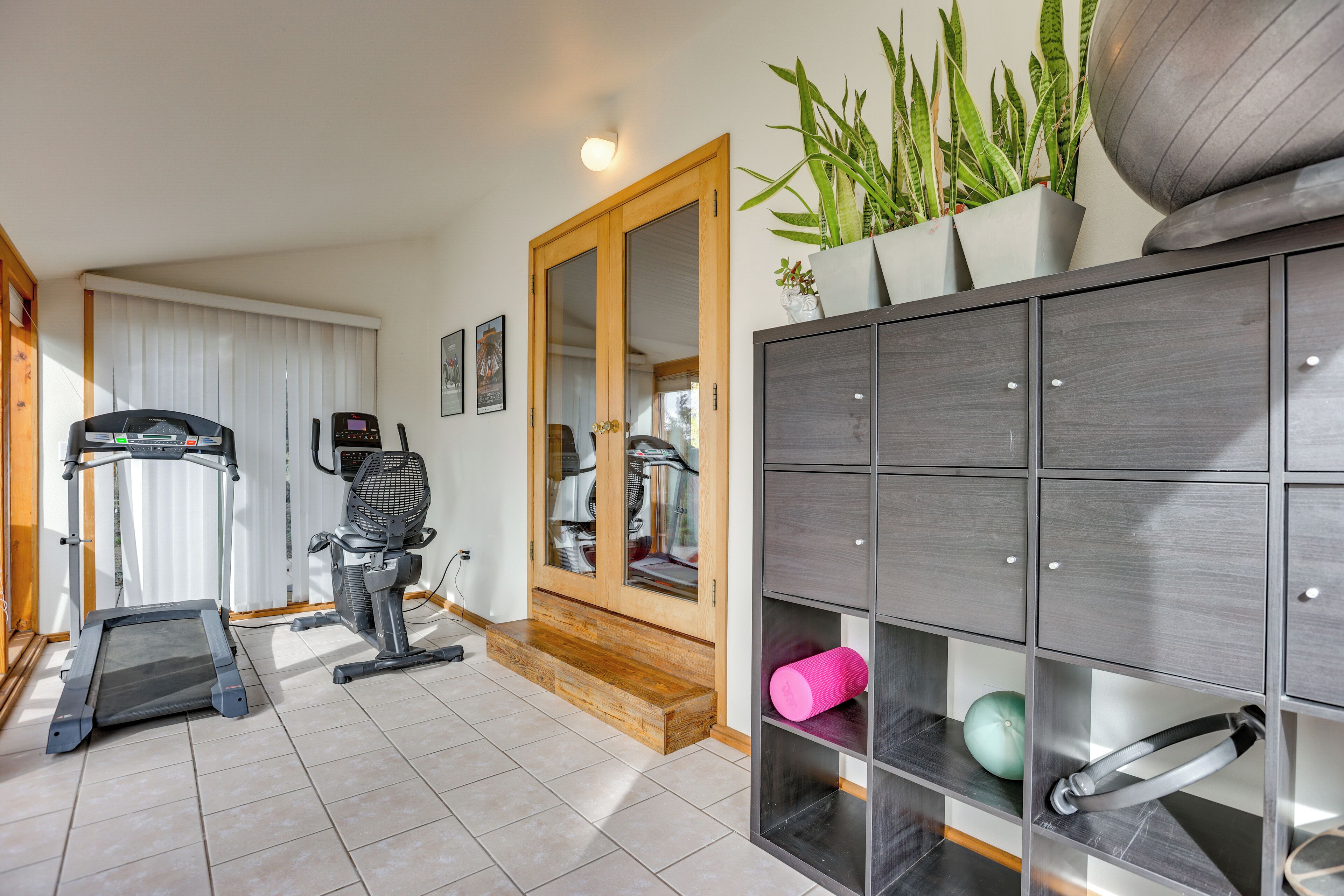 A home gym with a treadmill, exercise bike, and weights, a wooden door, and a mirrored closet with shelves.