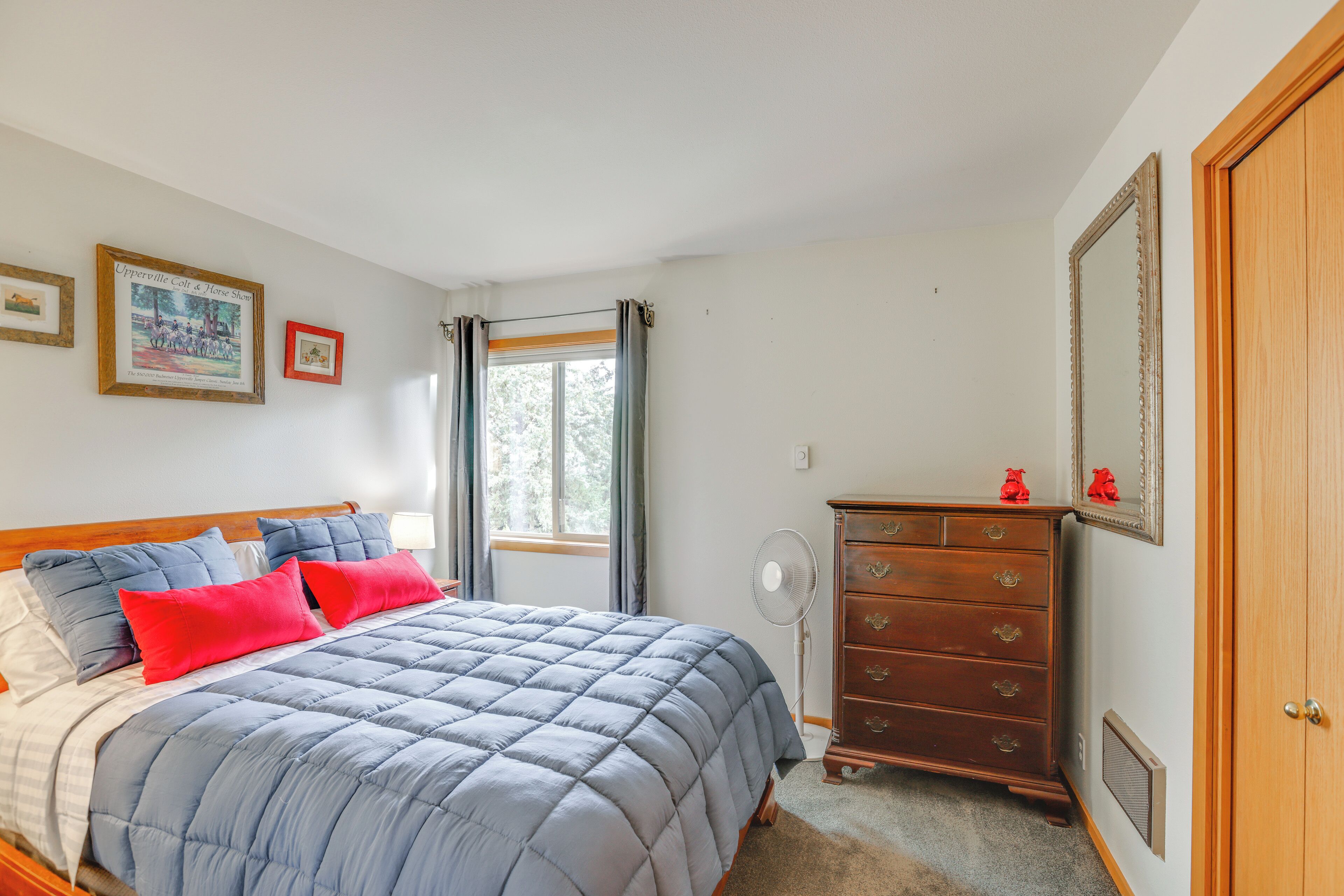A bedroom with a bed, a dresser, a mirror, and a window with curtains.