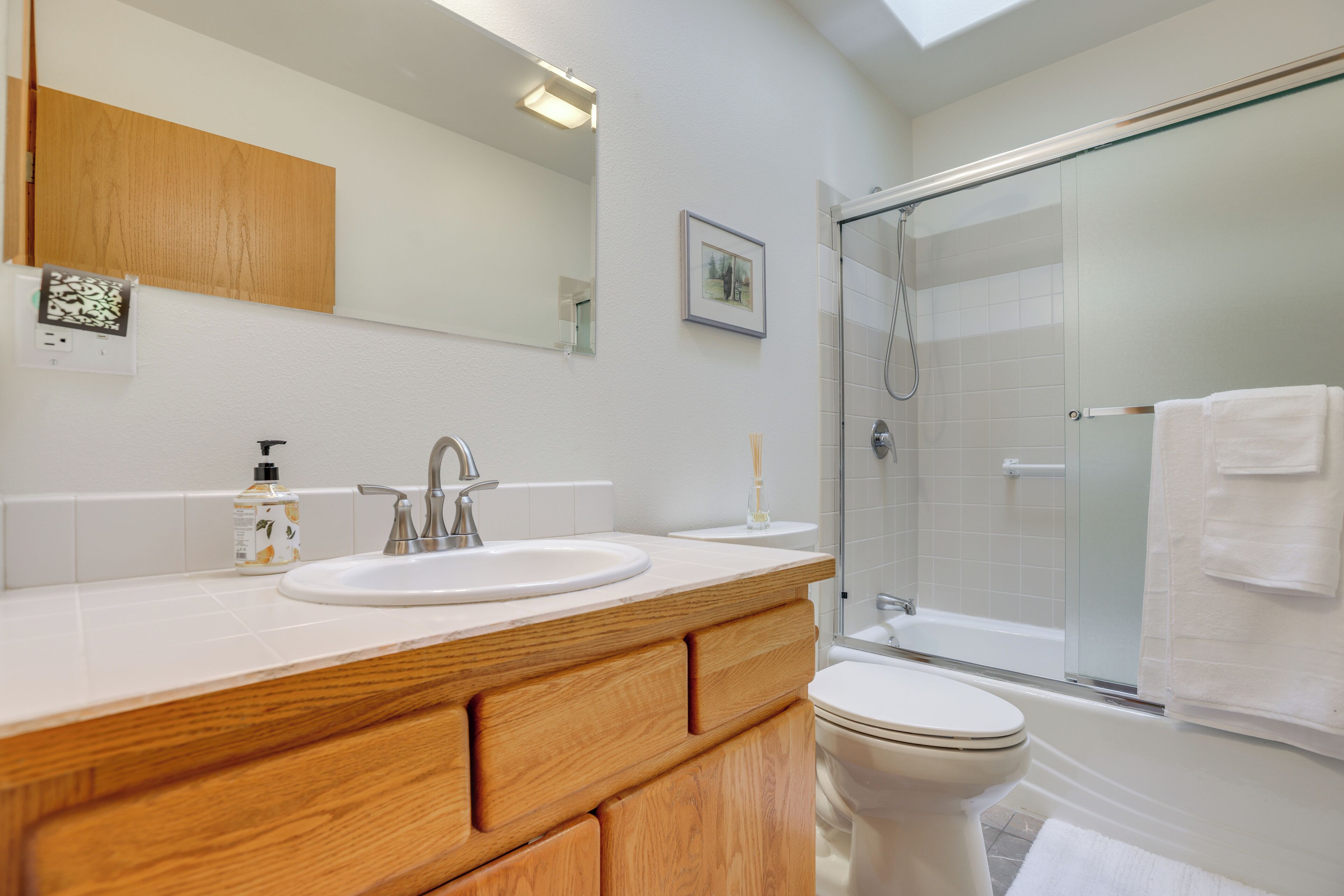 A modern bathroom with a wooden vanity, two sinks, a toilet, and a glass-enclosed shower.