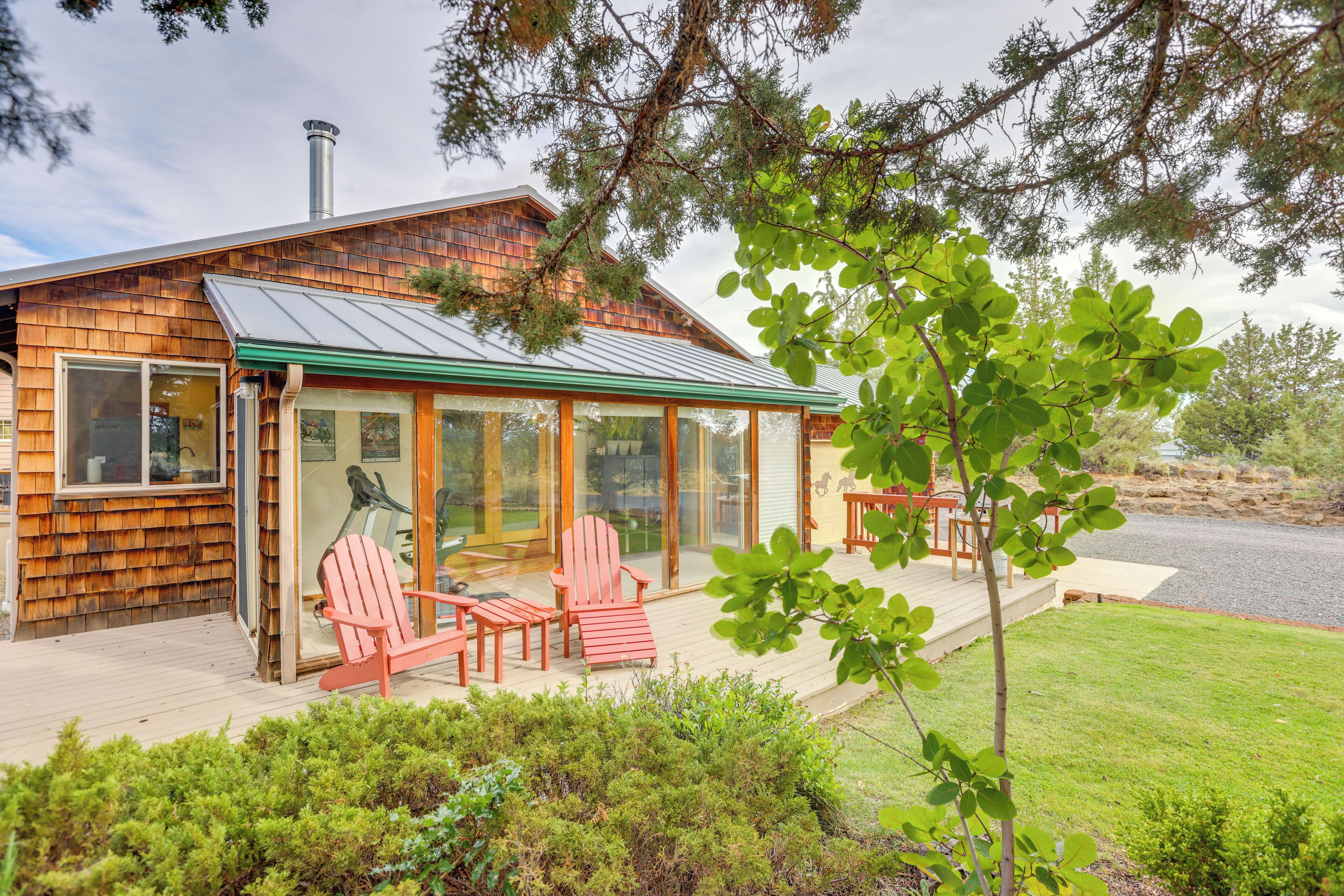 A wooden cabin with a glass-enclosed porch, red Adirondack chairs, and a view of the surrounding landscape.
